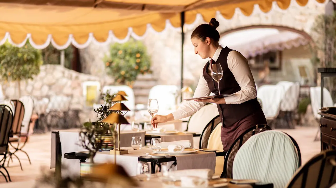 A waiter setting tables on the shaded restaurant terrace.