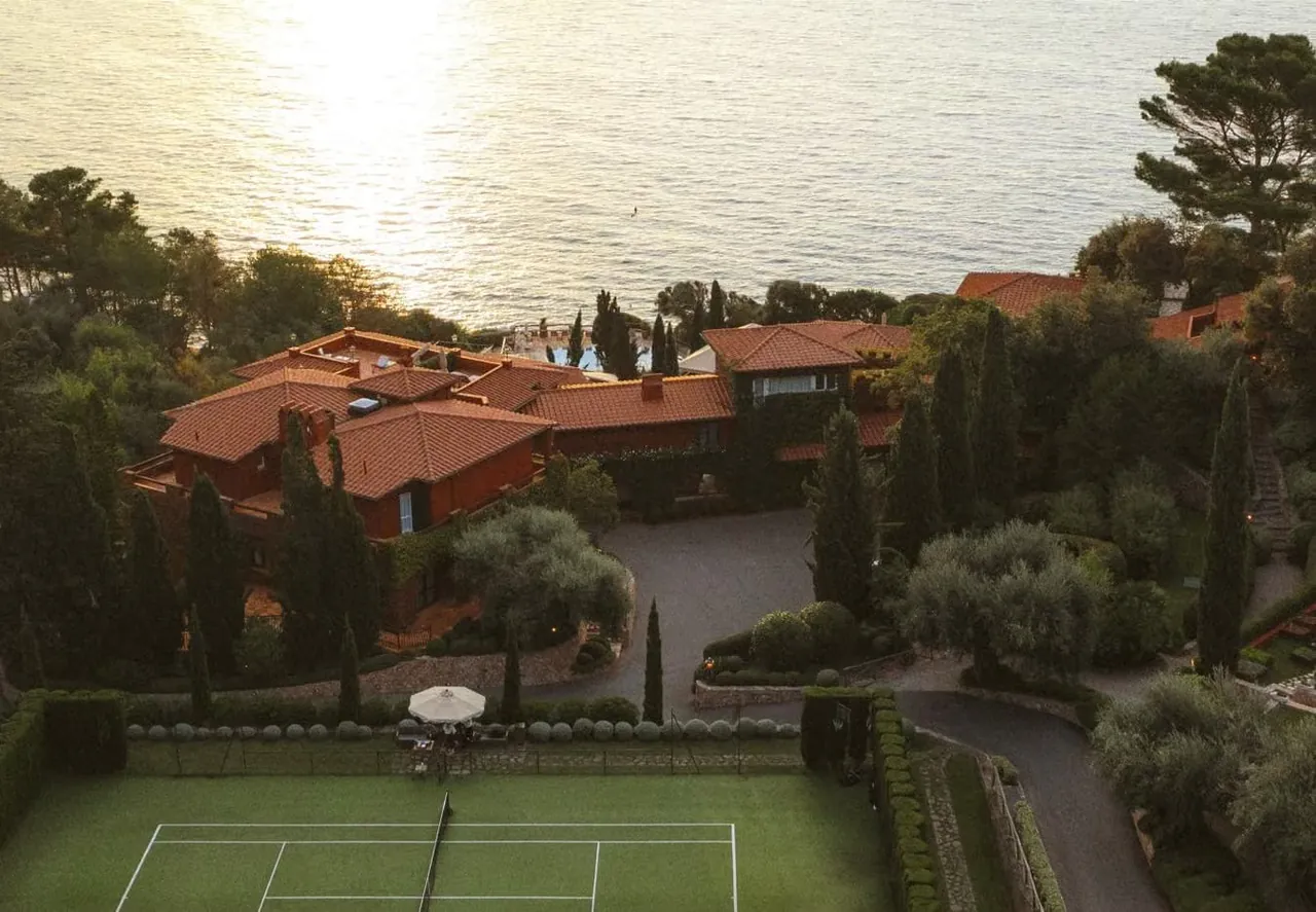 The hotel buildings and tennis court among pine trees at sunset.