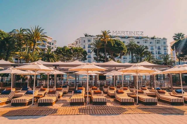 Rows of sunbeds and parasols on the private beach with the hotel facade behind.