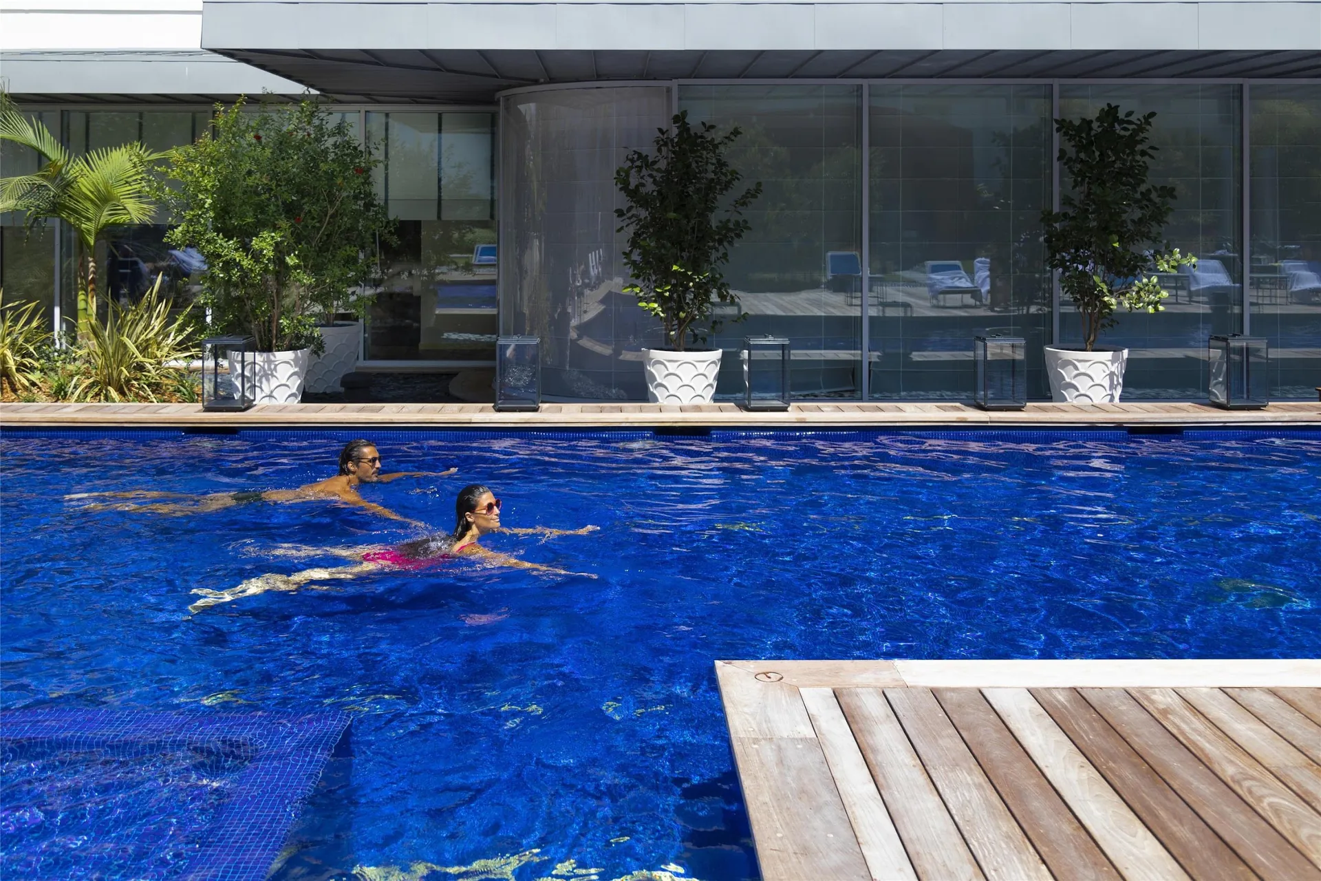 Guests swimming in the large outdoor pool beside a wooden deck.