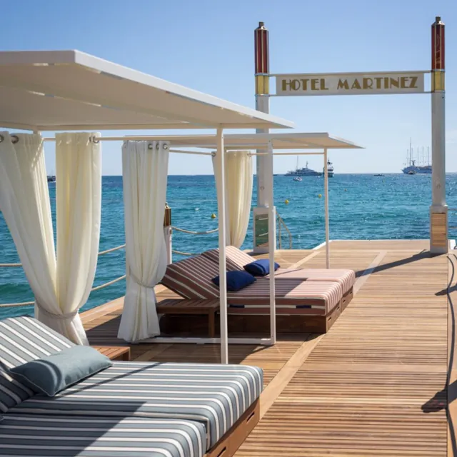 Cabanas with white curtains on the wooden jetty of the hotel beach club.