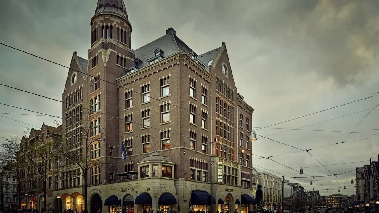 The red brick facade of Hotel TwentySeven on Dam Square under a cloudy sky.