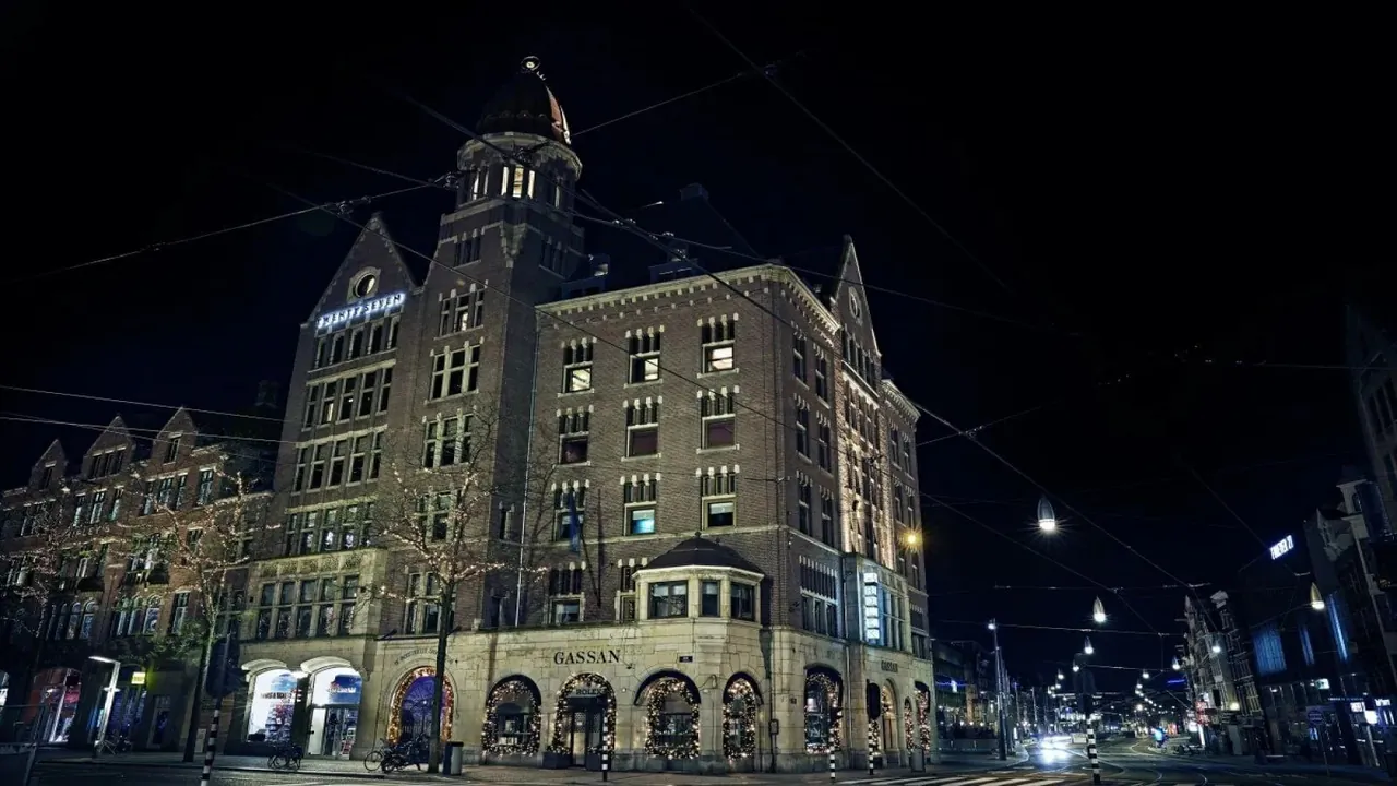The hotel building lit up on Dam Square at night.