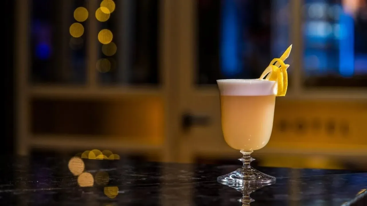 A golden cocktail garnished with citrus on a dark marble table.
