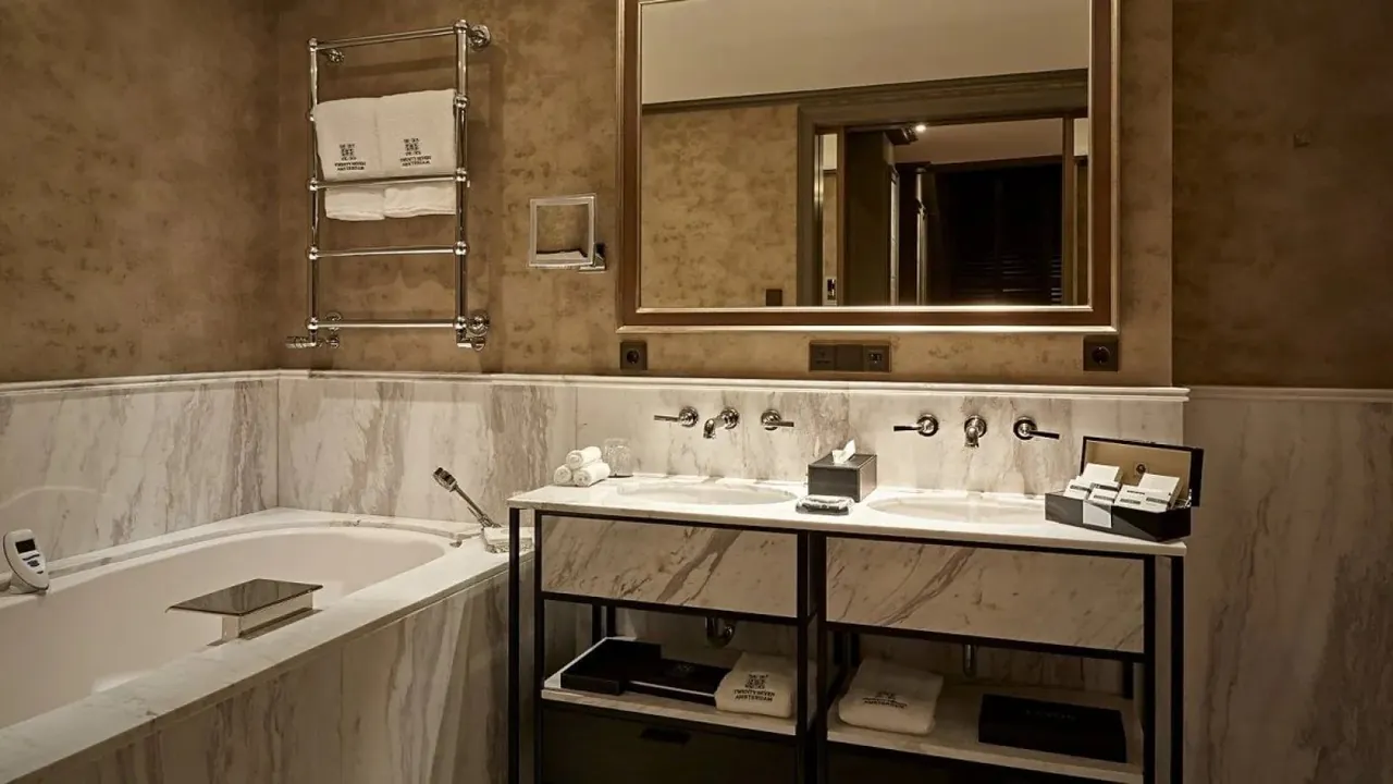 A marble bathroom with a bathtub and a double washbasin.