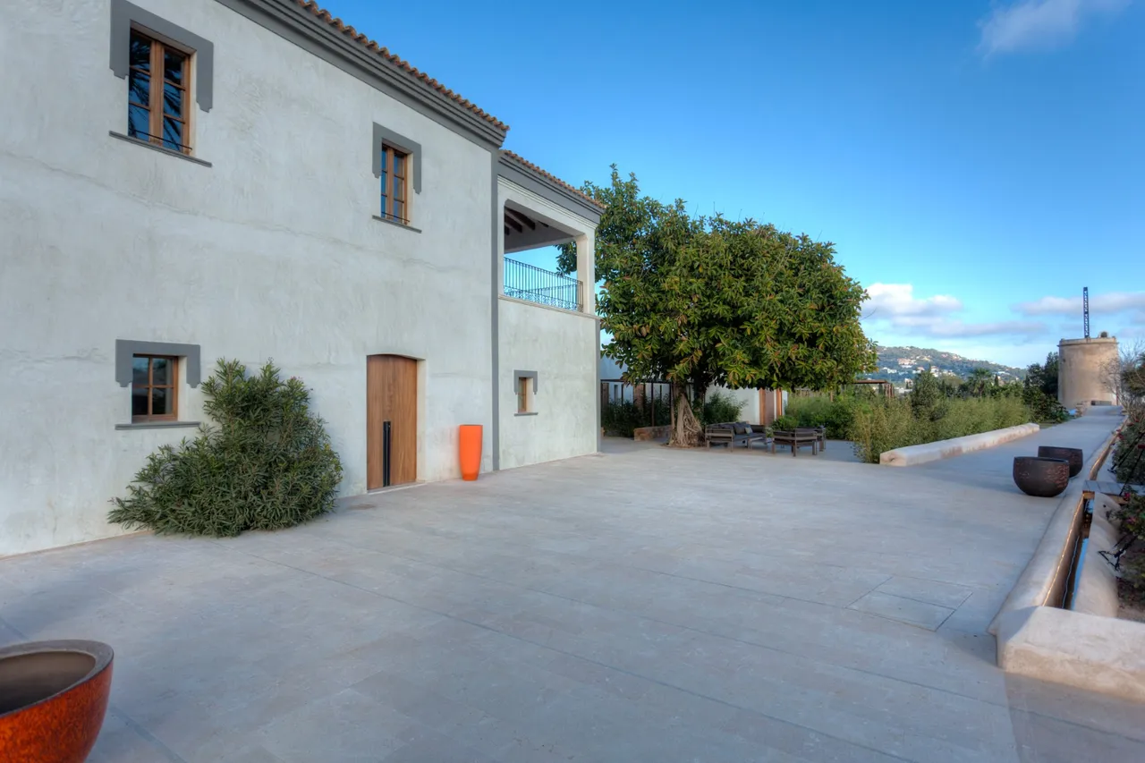 Whitewashed farmhouse building and stone courtyard at Hotel Xereca, Ibiza, with an orange tree and hills