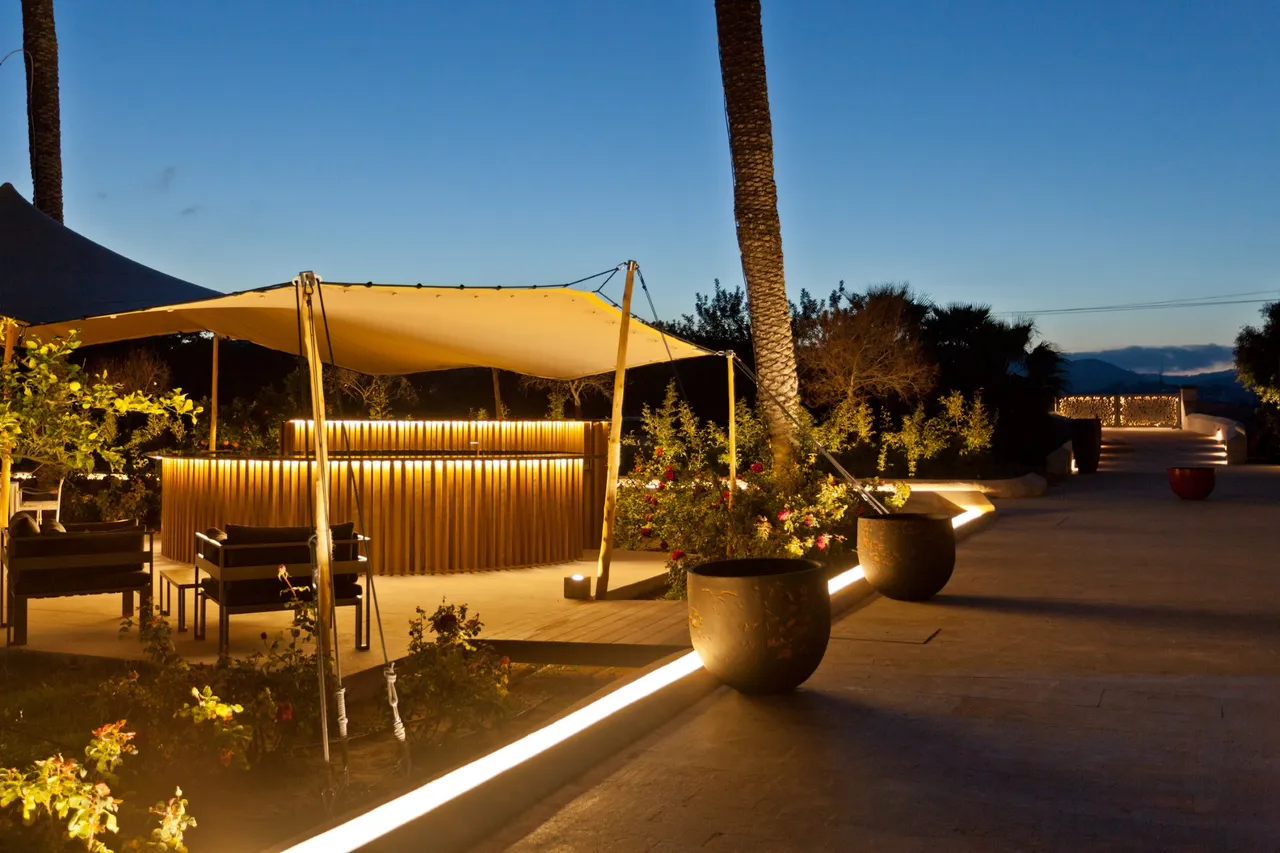 Garden bar at Hotel Xereca, Ibiza, at dusk with a canvas sail, palm trees and lit planters