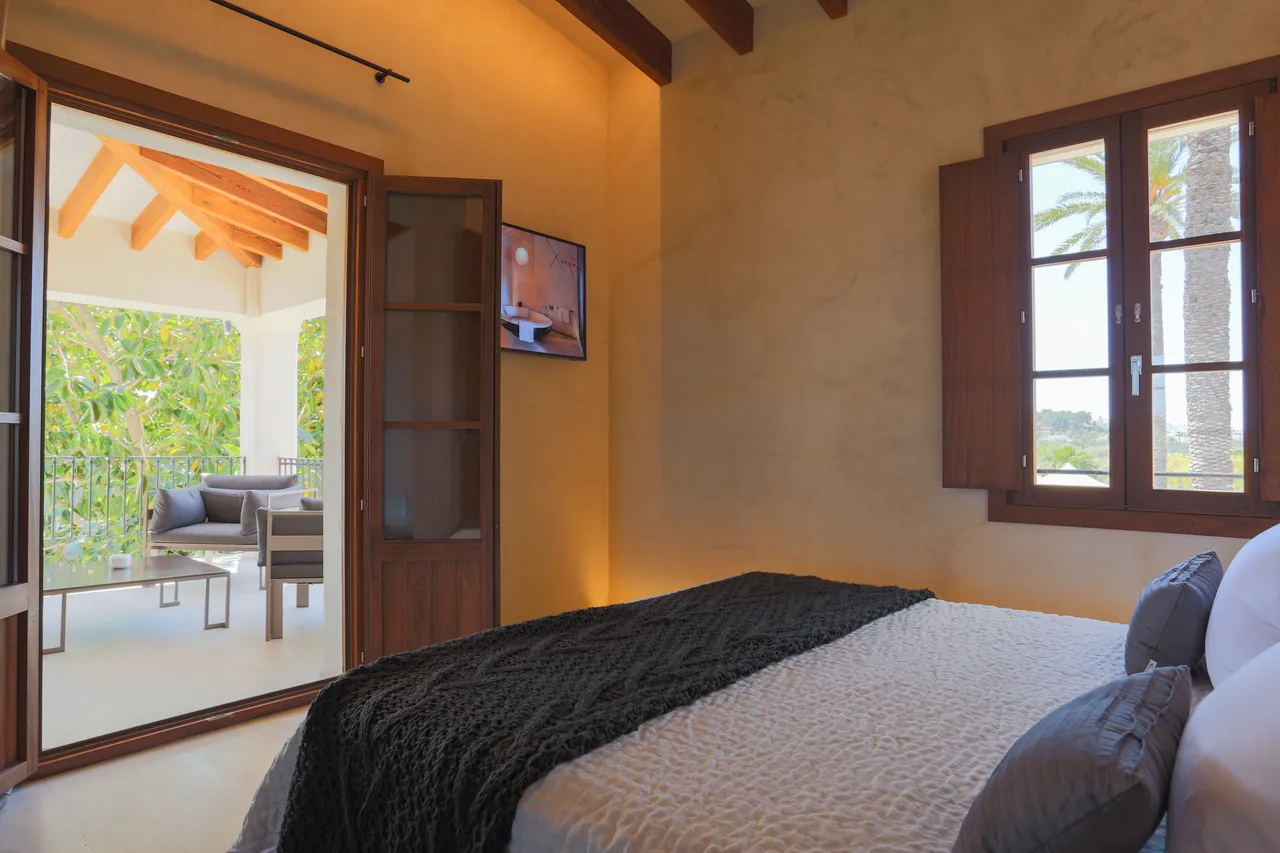 Bedroom at Hotel Xereca, Ibiza, with timber beams and doors opening onto a shaded terrace with sofas