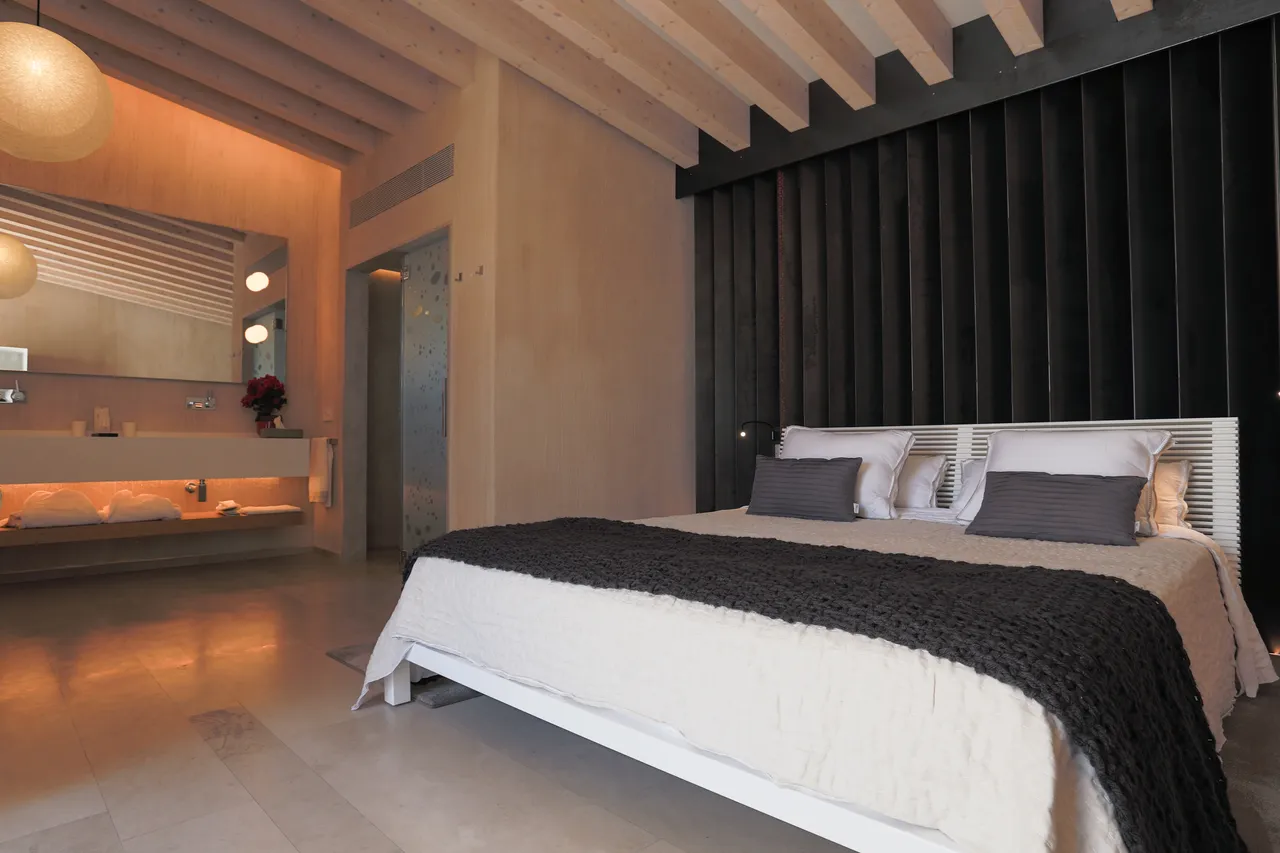 Bedroom at Hotel Xereca, Ibiza, with a black slatted wall, white bed, knitted throw and open-plan basin