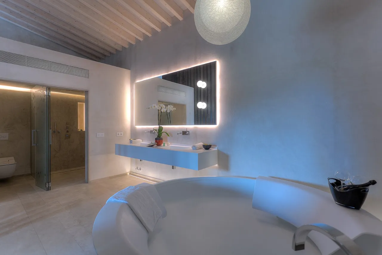 Bathroom at Hotel Xereca, Ibiza, with a round freestanding tub, backlit mirror and wooden ceiling beams