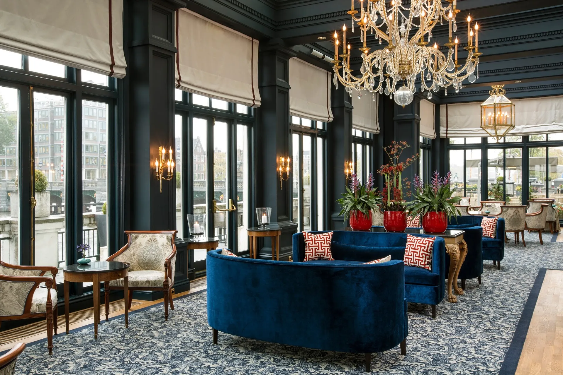 Tall windows, blue velvet seating and a candle chandelier in a lounge at the InterContinental Amstel Hotel