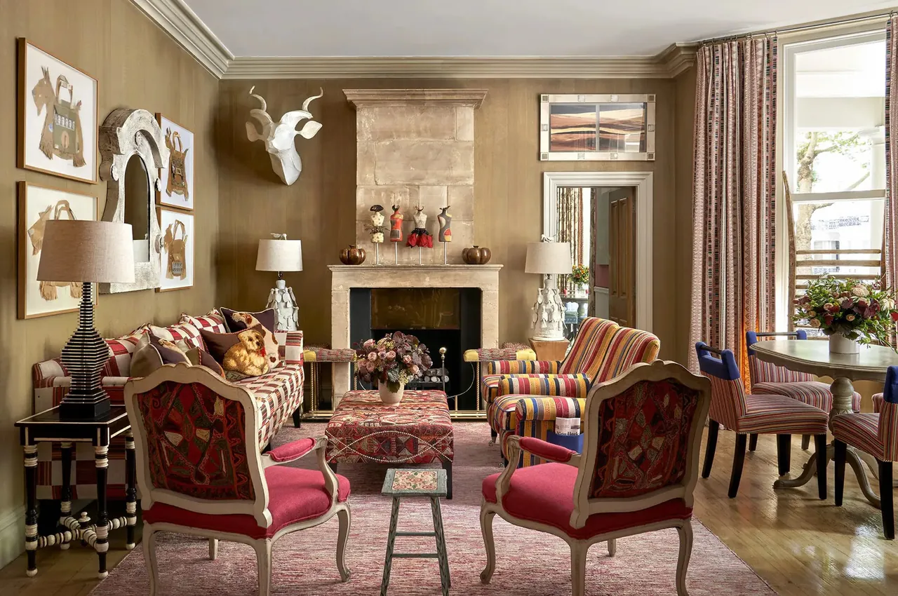Drawing room with red armchairs gathered around a fireplace and folk art on the walls.