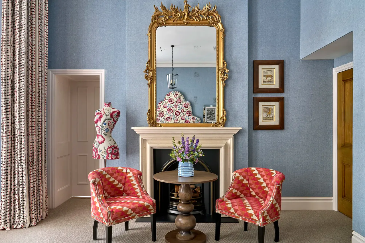 Junior suite sitting area with red armchairs and a gilt mirror over the fireplace.