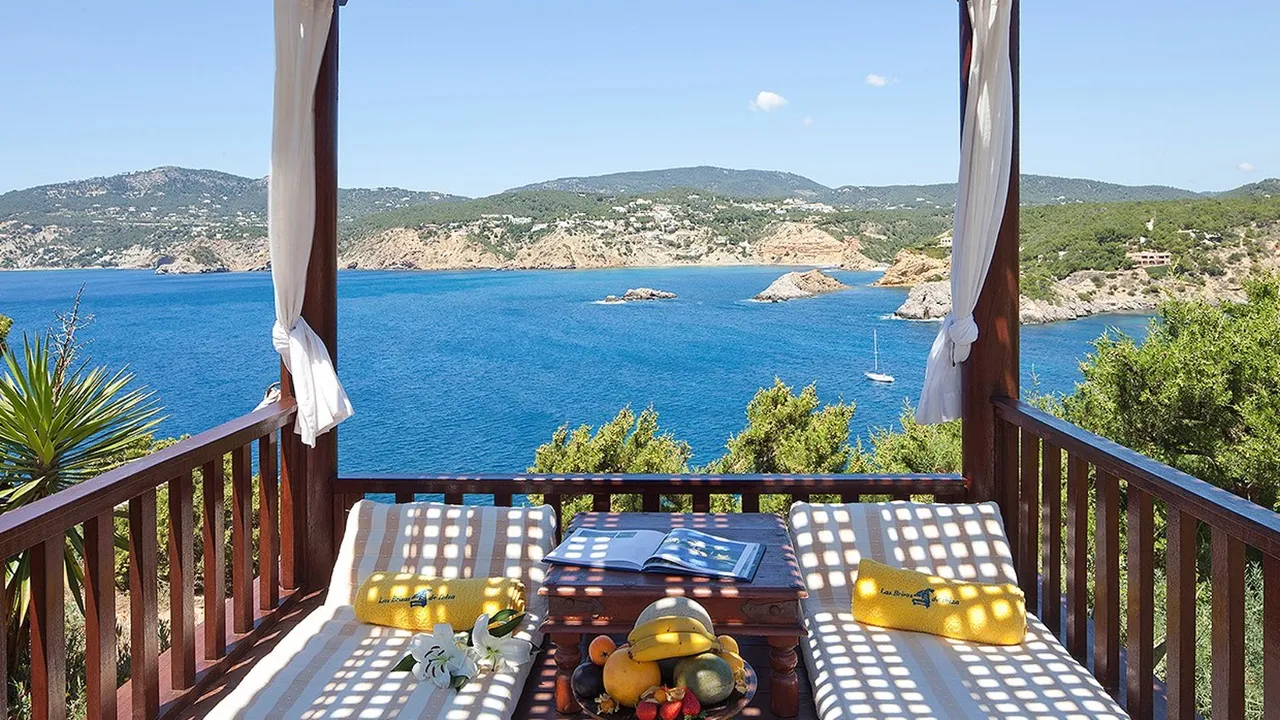 Wooden balcony at Las Brisas with two daybeds and fruit, overlooking a blue bay and green hills