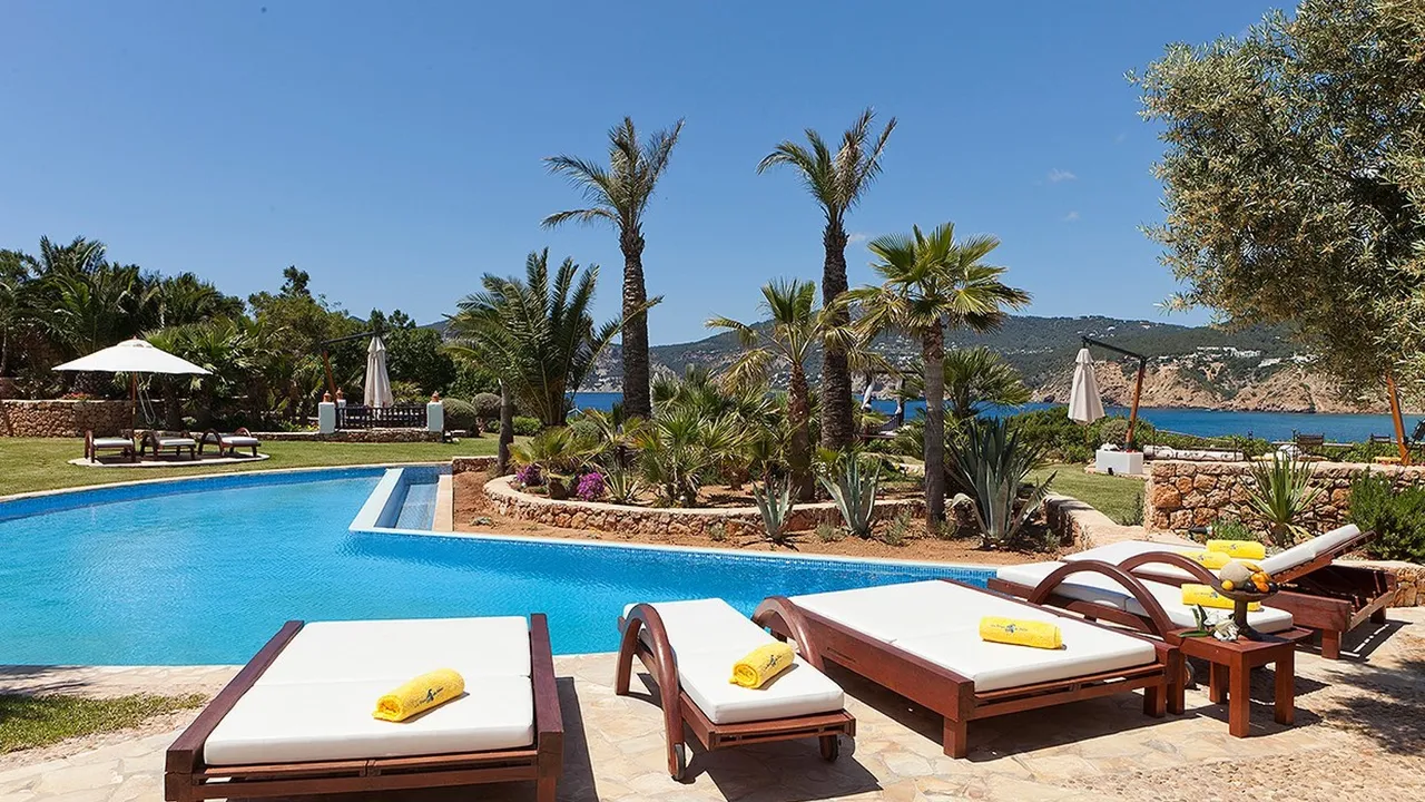 Pool area at Las Brisas with white sun loungers, palm trees and views over the sea and hills