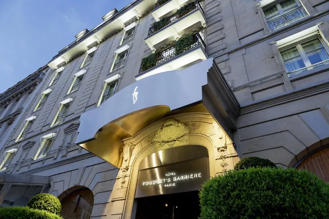 Entrance of Le Fouquet's Barriere, Paris, with a curved canopy on a Haussmann stone facade at dusk