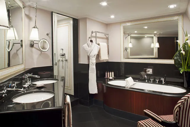Marble bathroom at Le Fouquet's Barriere with double basins, a wood-panelled bathtub and a hanging bathrobe