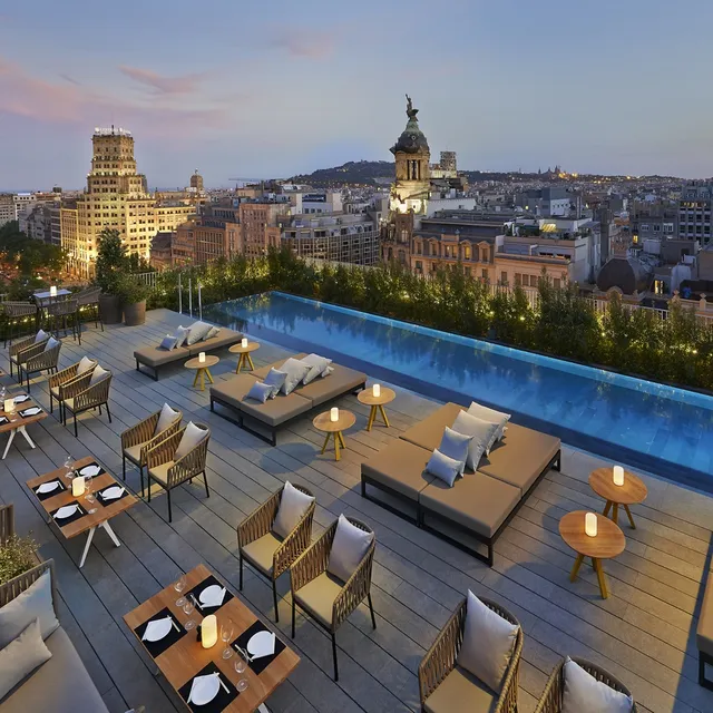 Rooftop pool terrace at Mandarin Oriental, Barcelona, at dusk with daybeds, candlelit tables and city views
