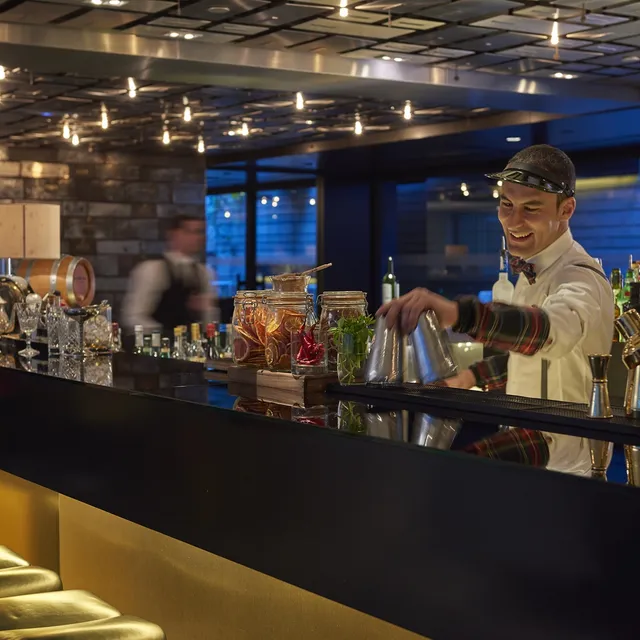 Bartender at the black bar counter of Mandarin Oriental, Barcelona, with infusion jars and gold stools