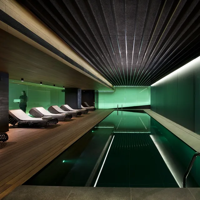 Indoor pool at Mandarin Oriental, Barcelona, with green-lit walls, a slatted ceiling and woven loungers