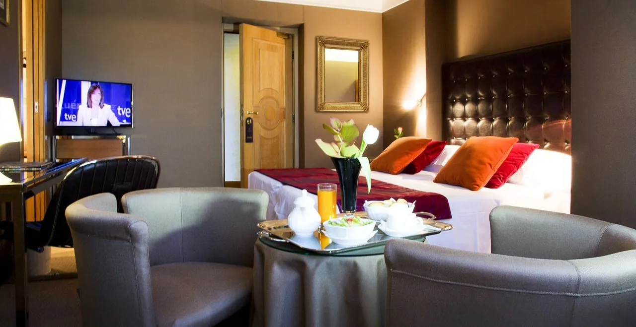 A room with armchairs and a breakfast tray by the bed.
