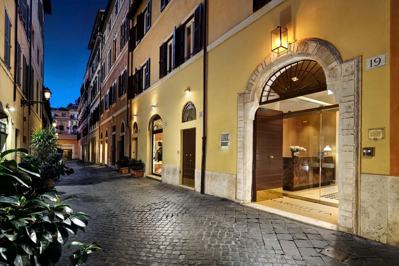 The arched stone entrance of Margutta 19 on the cobbled Via Margutta at night.