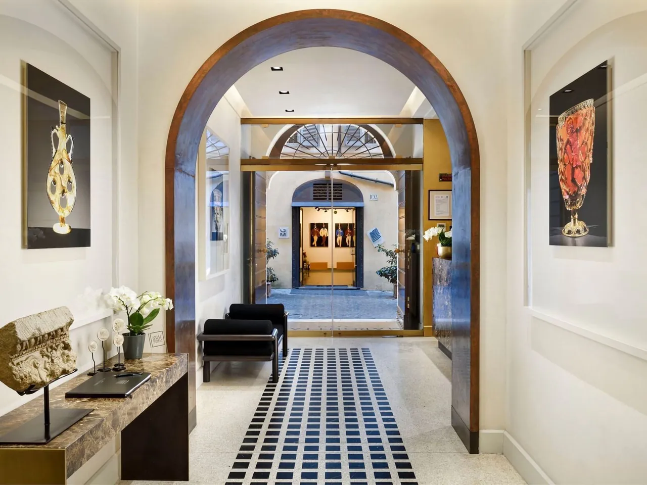 A marble hallway with an arched doorway and framed art leading through the hotel.