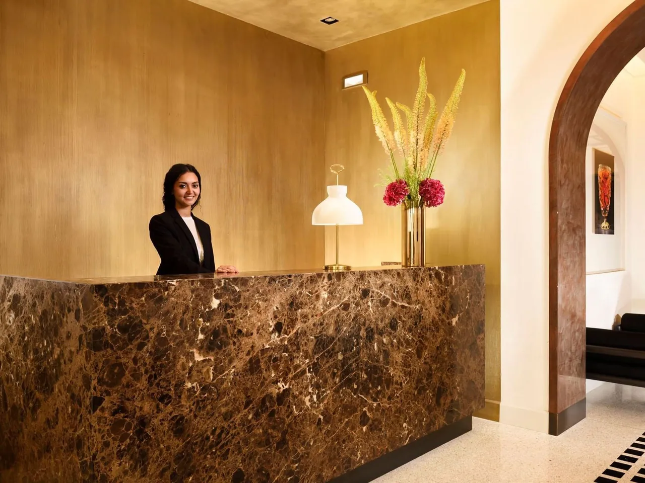 The marble reception desk with a tall flower arrangement and a receptionist.