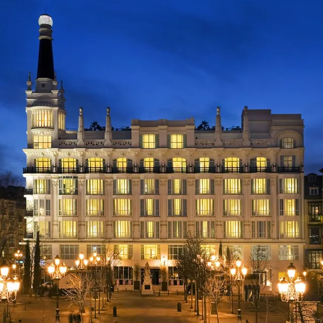 White facade of ME Madrid lit at night, with a black-spired tower above a square with street lamps
