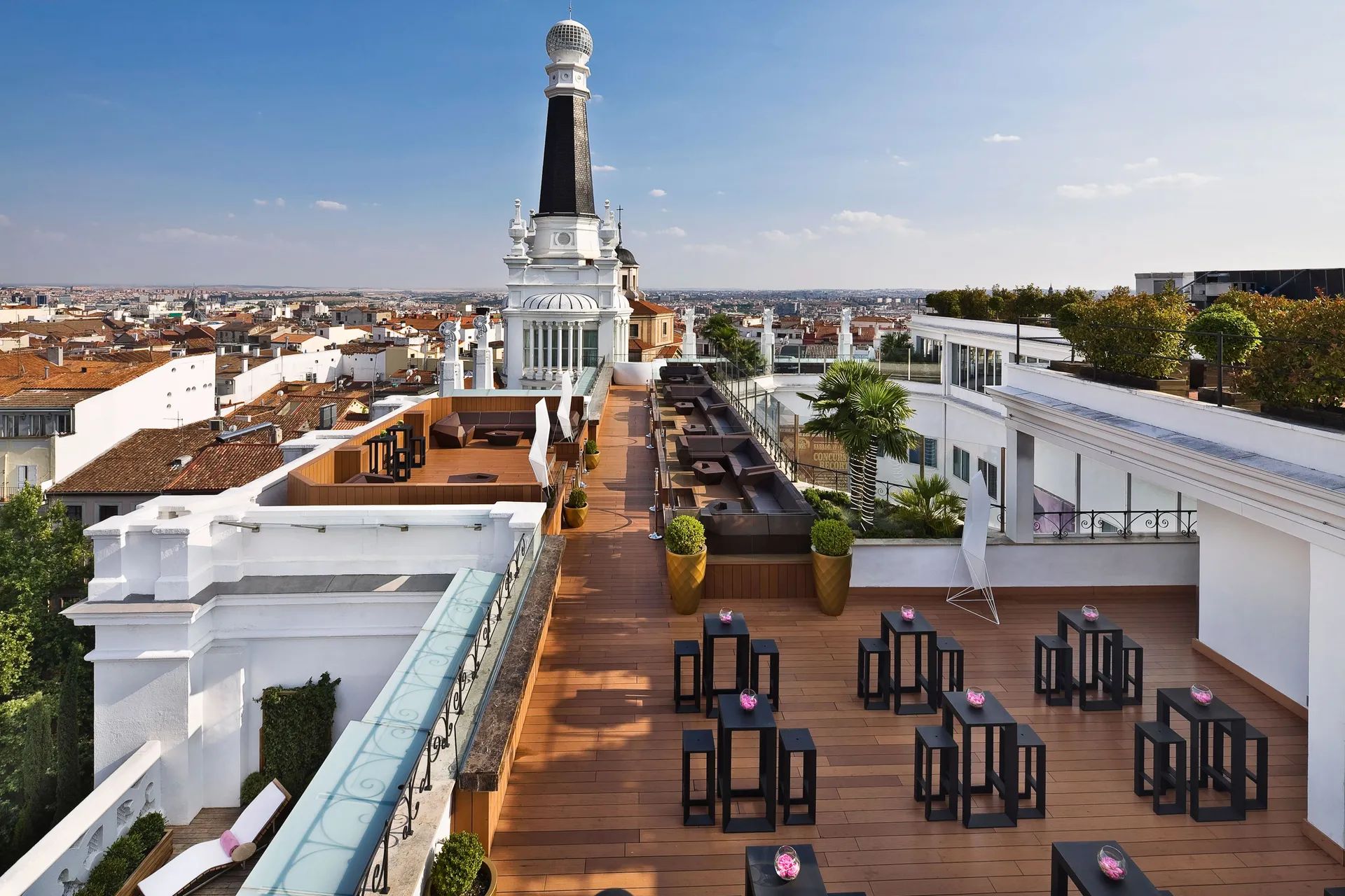 Rooftop terrace at ME Madrid with high tables, a wooden deck and the black spire against Madrid rooftops