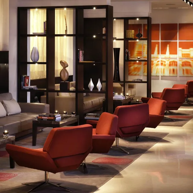 Lounge at ME Madrid with red swivel armchairs, grey sofas, lit shelving and orange city artwork