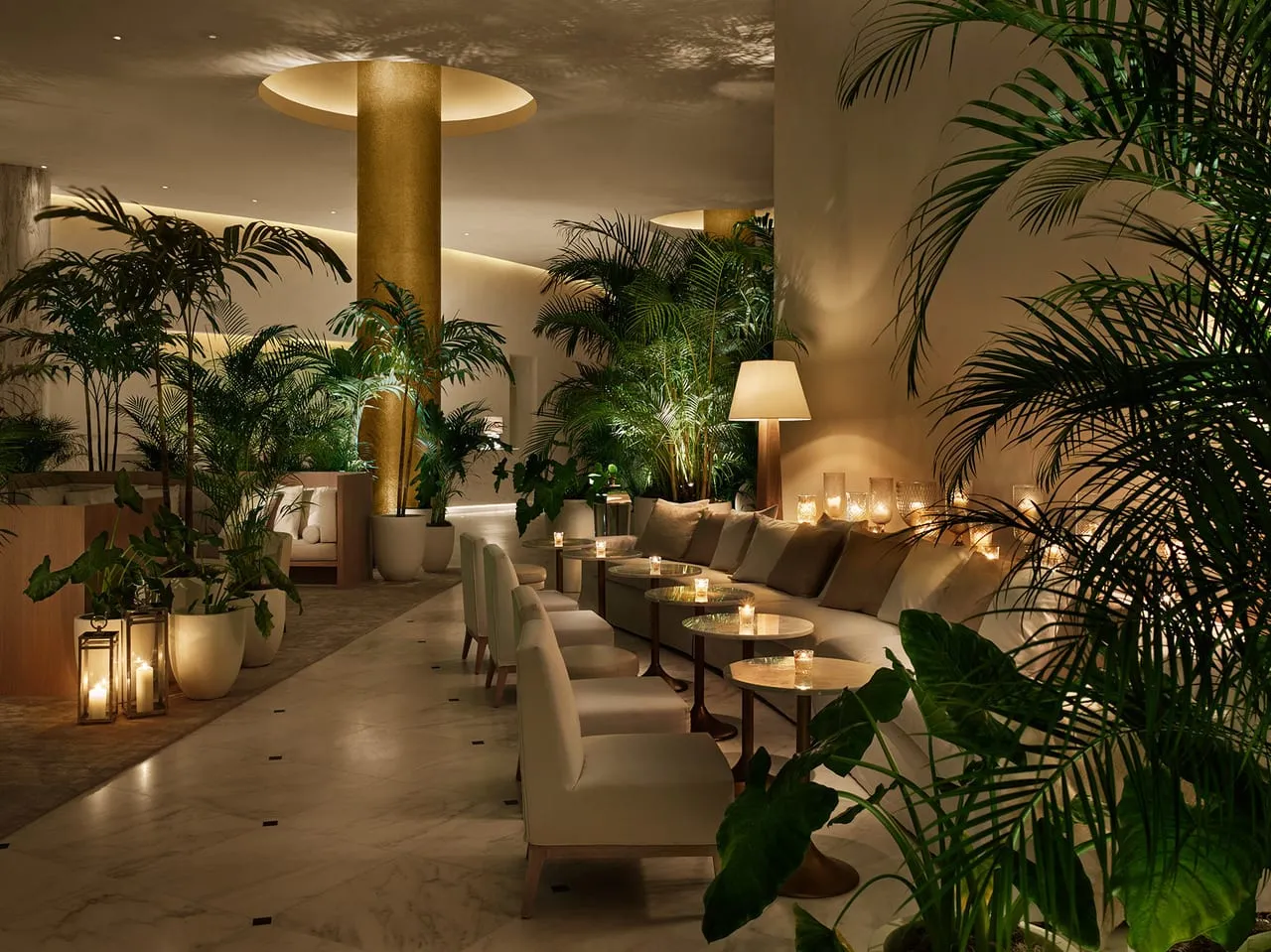 Lounge at The Miami Beach Edition with cream banquettes, candlelit tables, palms and a gold column