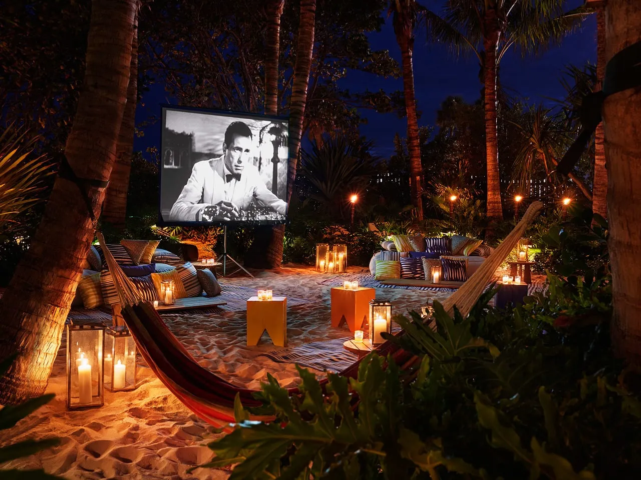 Outdoor cinema on the sand at The Miami Beach Edition with cushions, a hammock and lanterns under palms