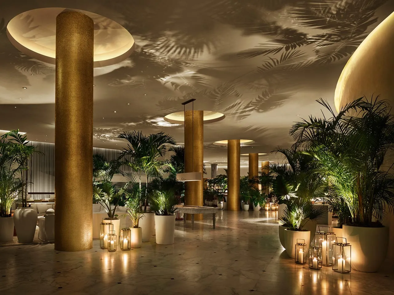 Lobby at The Miami Beach Edition with gold columns, potted palms, candle lanterns and palm leaf shadows