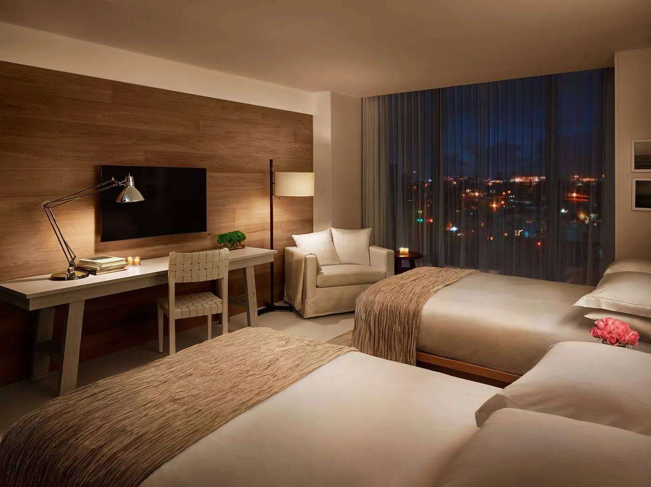 Twin room at The Miami Beach Edition with a wood-panelled wall, desk lamp and city lights at night