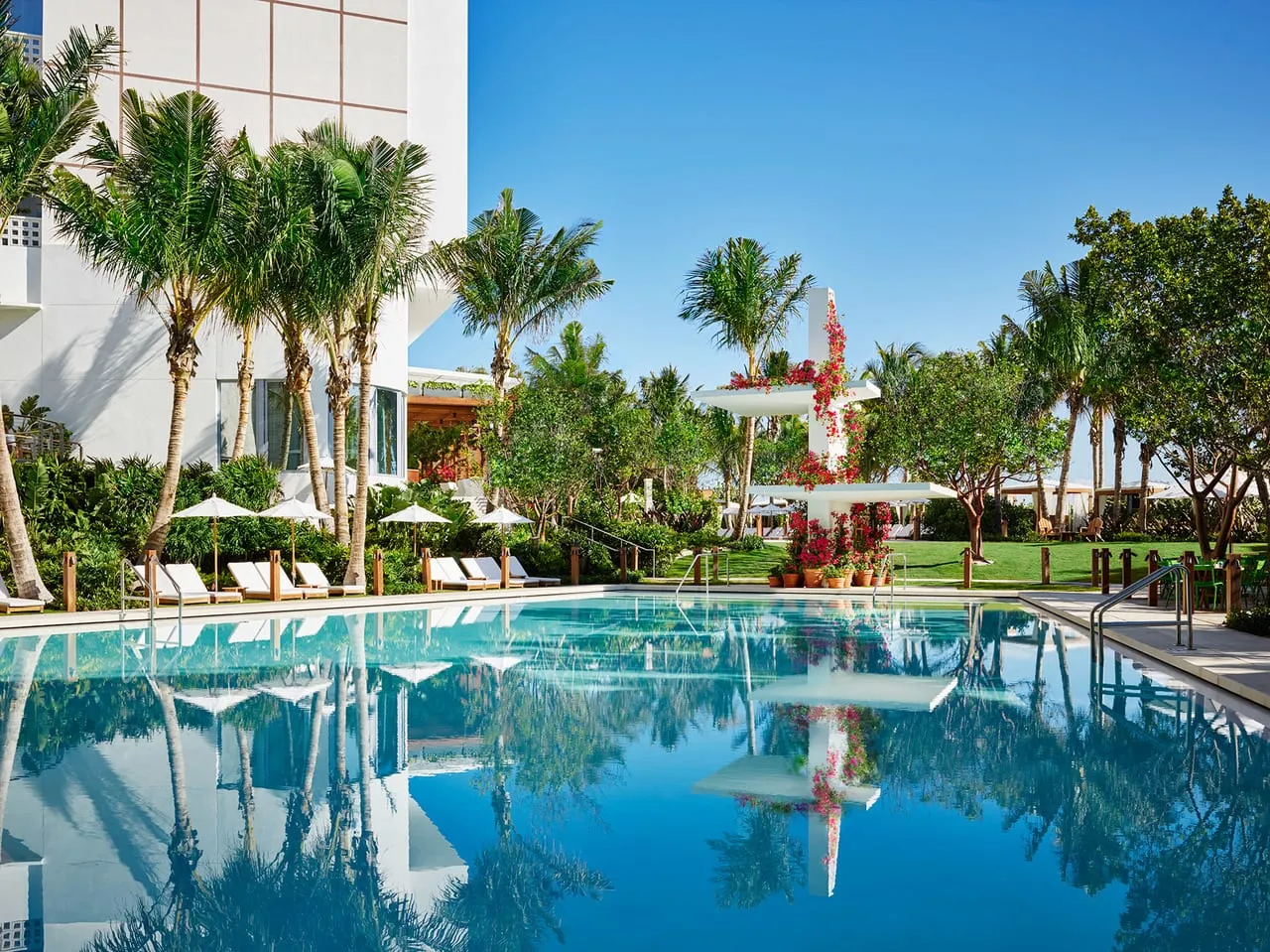Pool at The Miami Beach Edition with palm trees, white loungers and a tower hung with red flowers