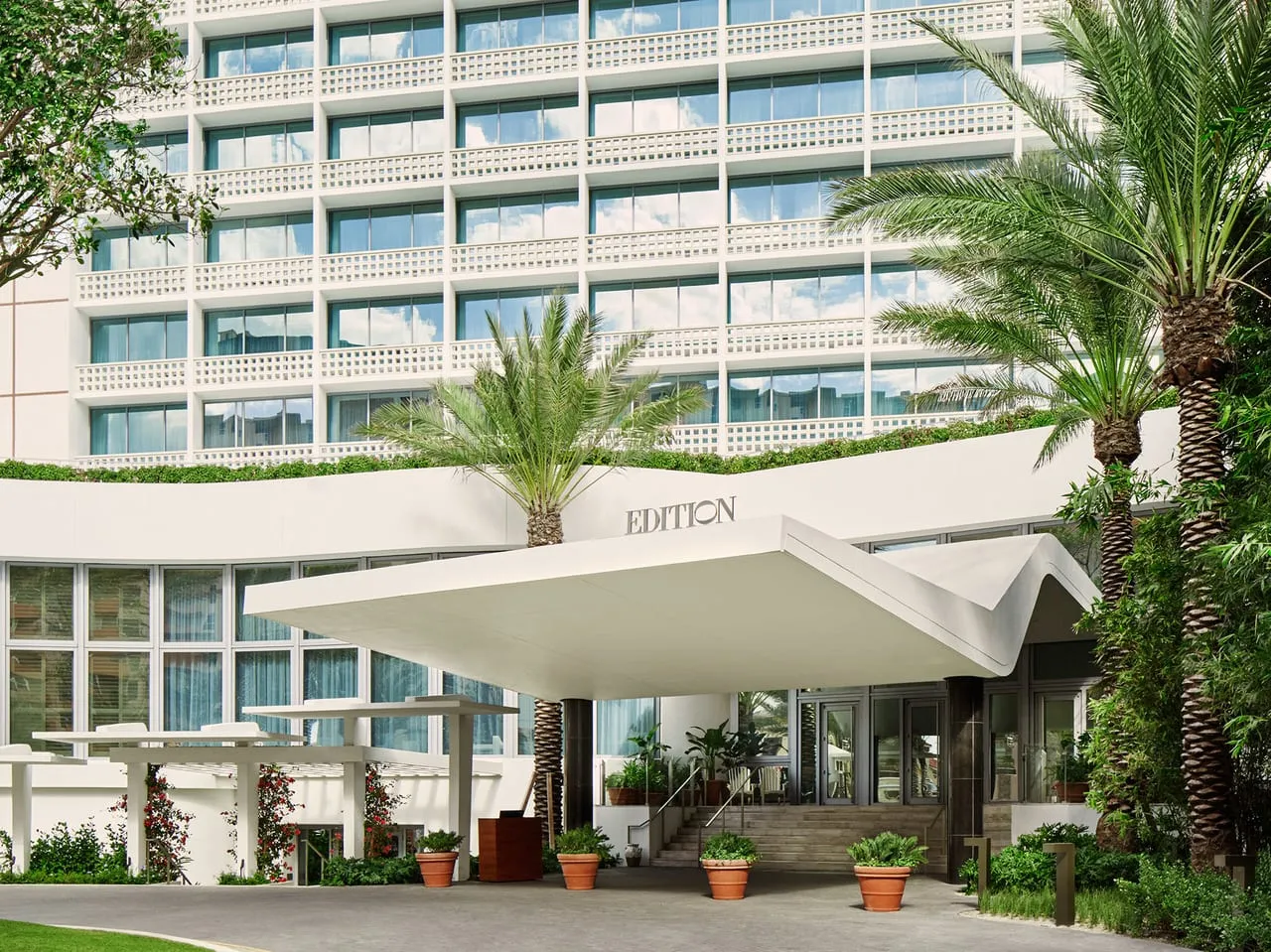 Entrance of The Miami Beach Edition with a white curved canopy, palm trees and a lattice-balconied tower