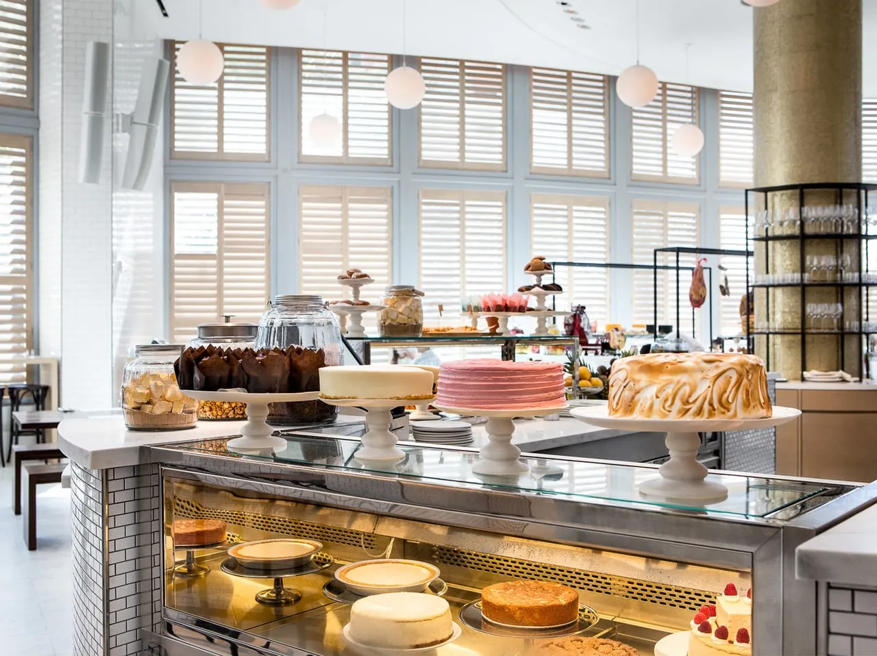 Pastry counter at The Miami Beach Edition with cakes on stands, a glass display case and shuttered windows