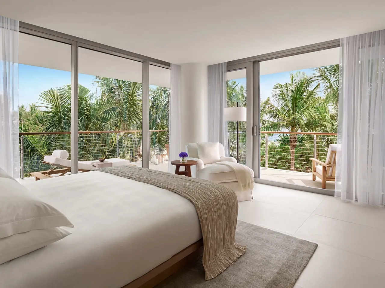 Bedroom at The Miami Beach Edition with floor-to-ceiling windows, a white armchair and palm tree views