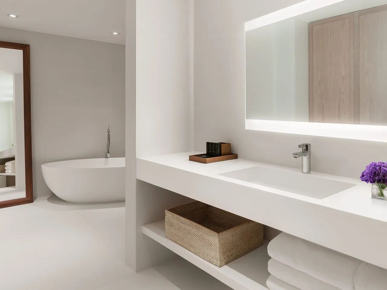 White bathroom at The Miami Beach Edition with a freestanding bathtub, backlit mirror and woven basket