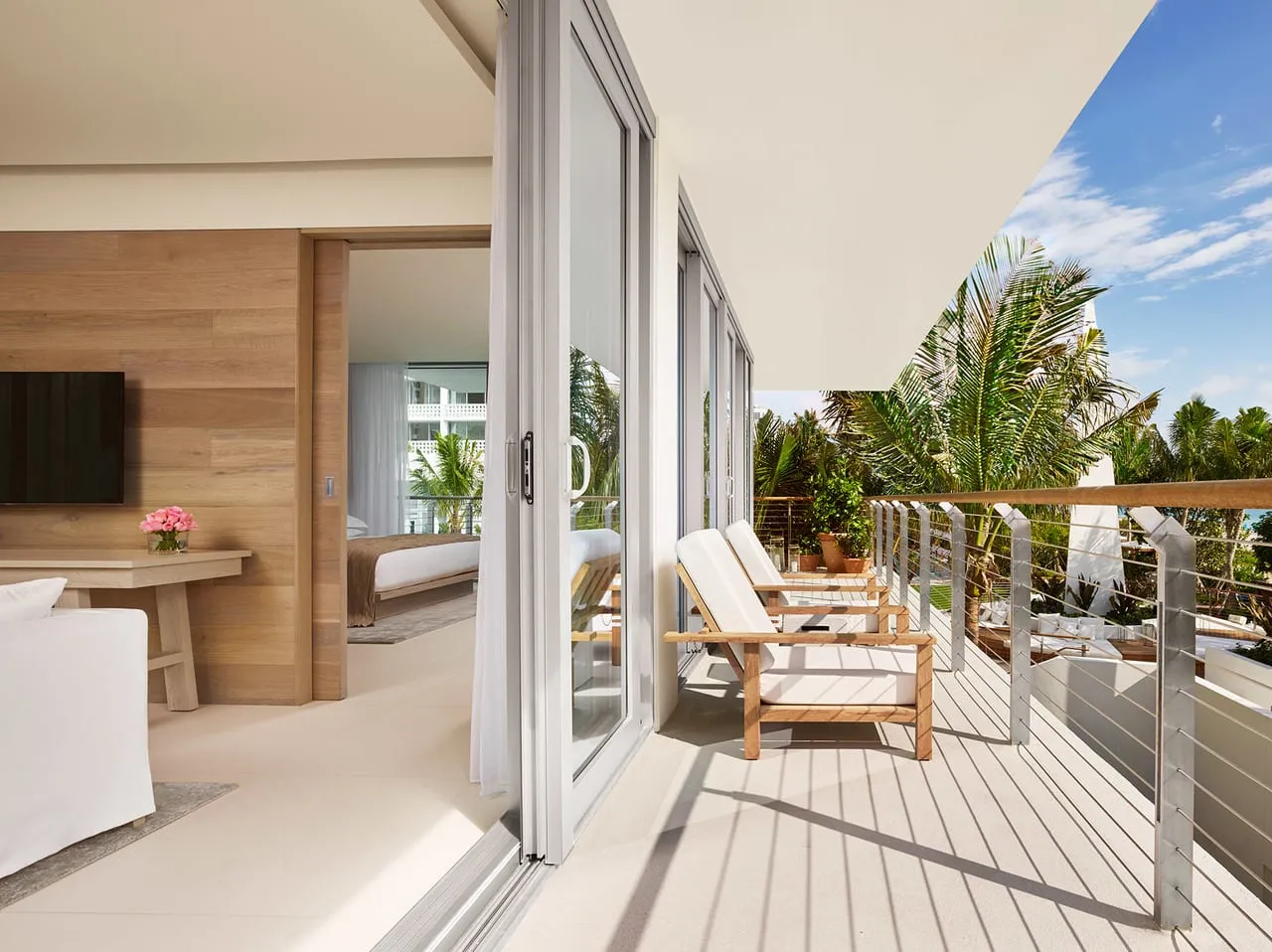 Suite balcony at The Miami Beach Edition with wooden loungers, glass sliding doors and palm trees
