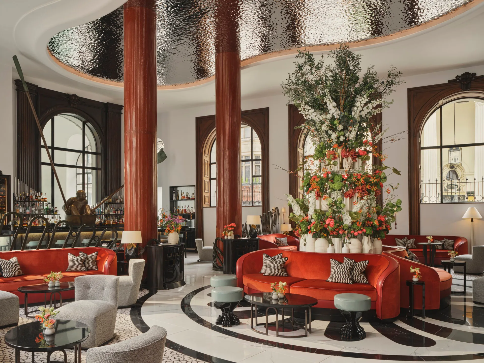 The lobby bar with red columns, arched windows and a tall floral display.