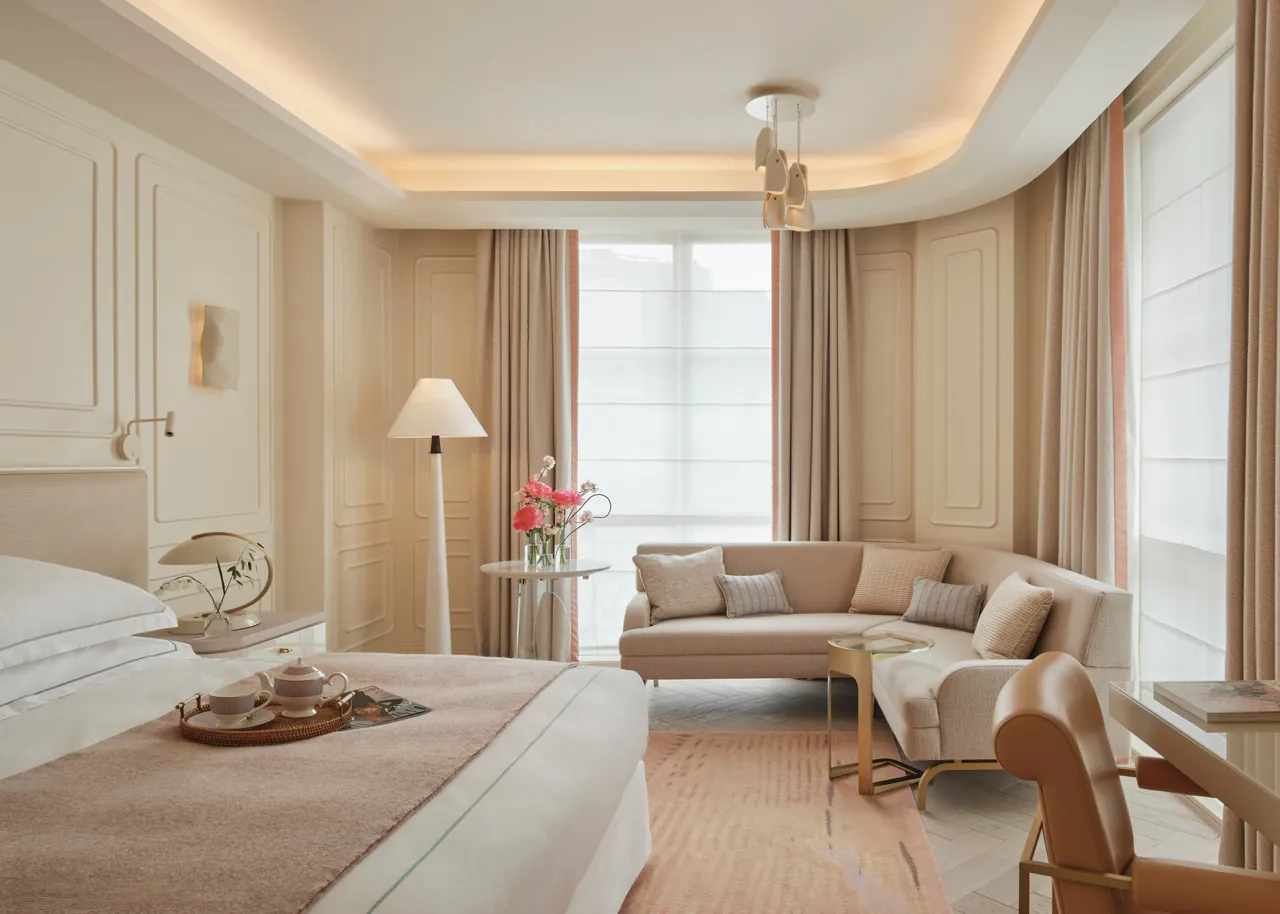 A bright deluxe room with a sofa, a reading chair and tall windows.
