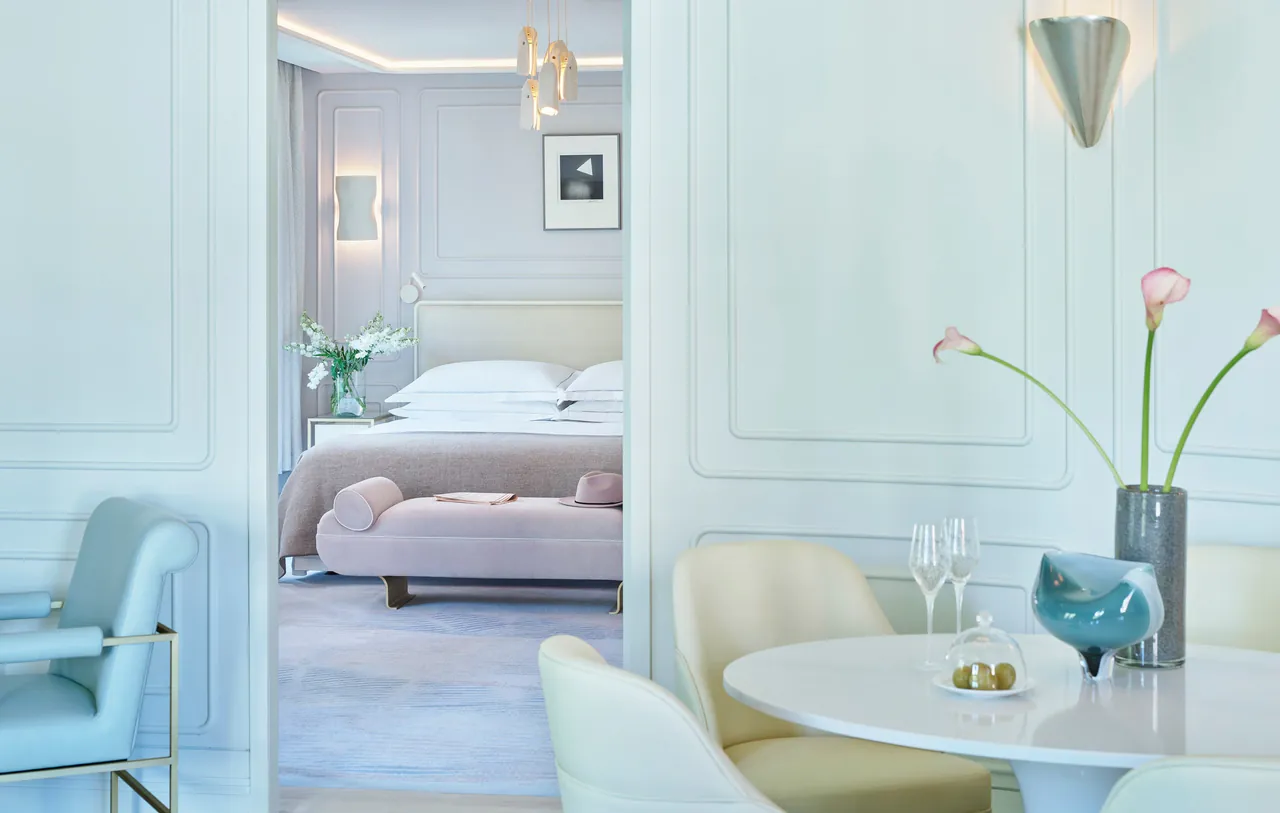A pale blue suite with a dining table and a bed in the background.