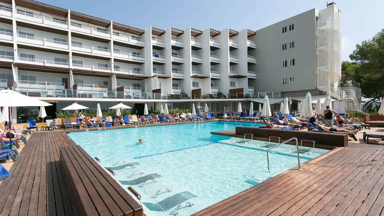 Busy pool deck at Palladium Hotel Don Carlos with wooden decking, blue loungers and white balconies