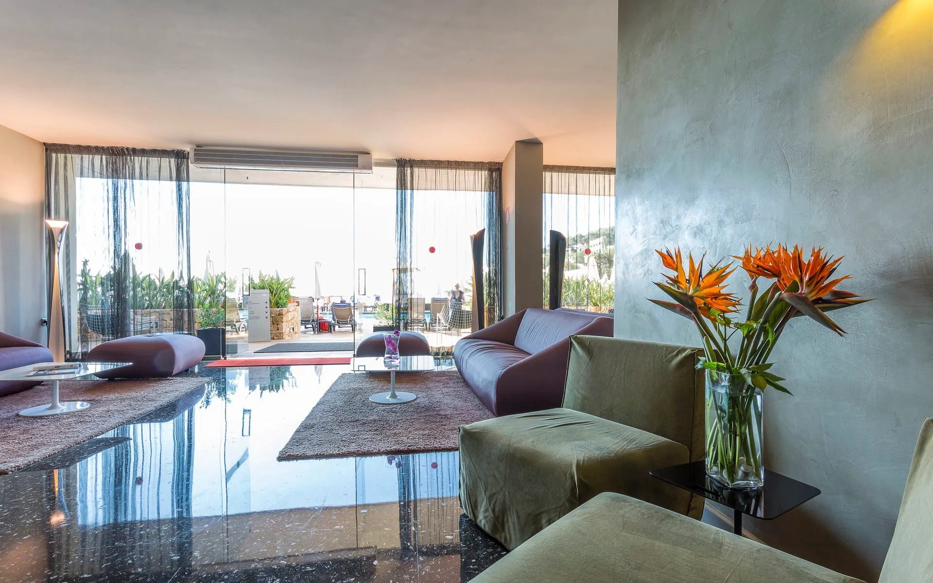 Lounge at Palladium Hotel Don Carlos with sofas, bird of paradise flowers and glass doors to a terrace