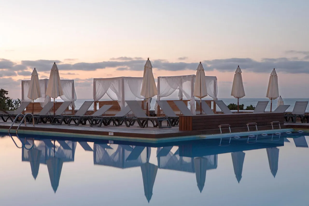Pool at Palladium Hotel Don Carlos at dusk, with curtained daybeds and parasols reflected in still water