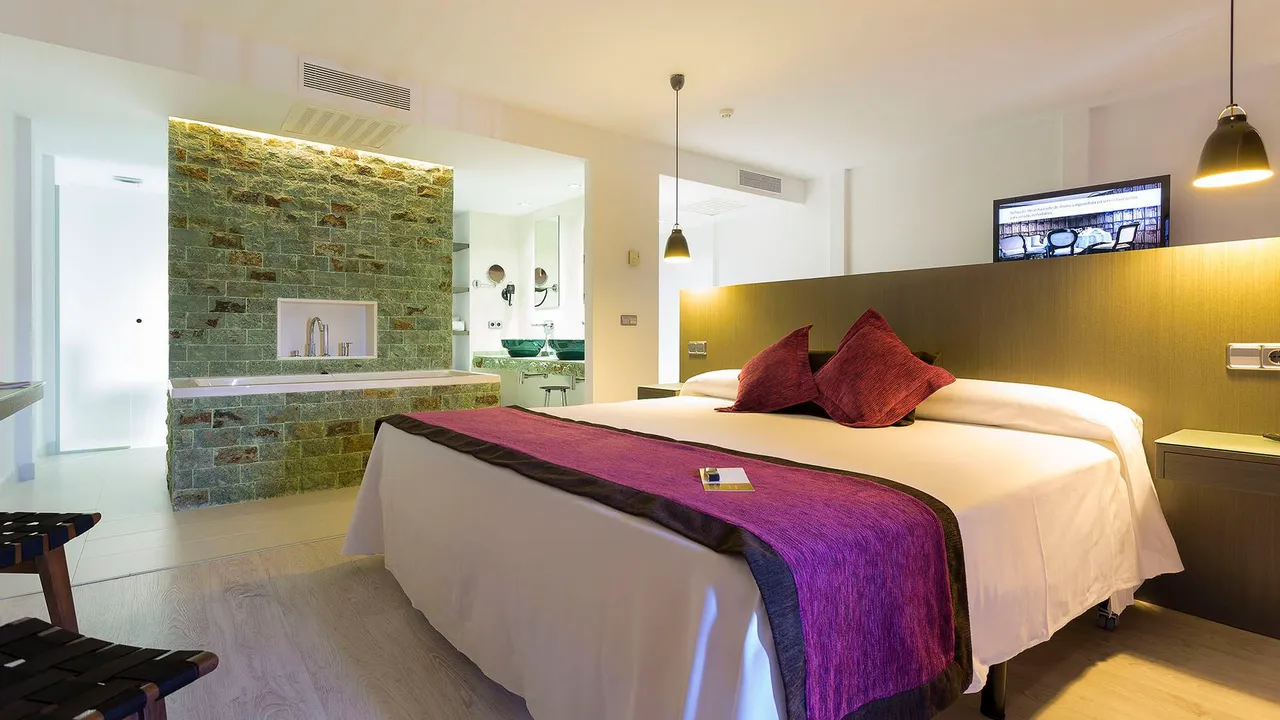 Room at Palladium Hotel Don Carlos with a purple bed runner, red cushions and green stone bath wall