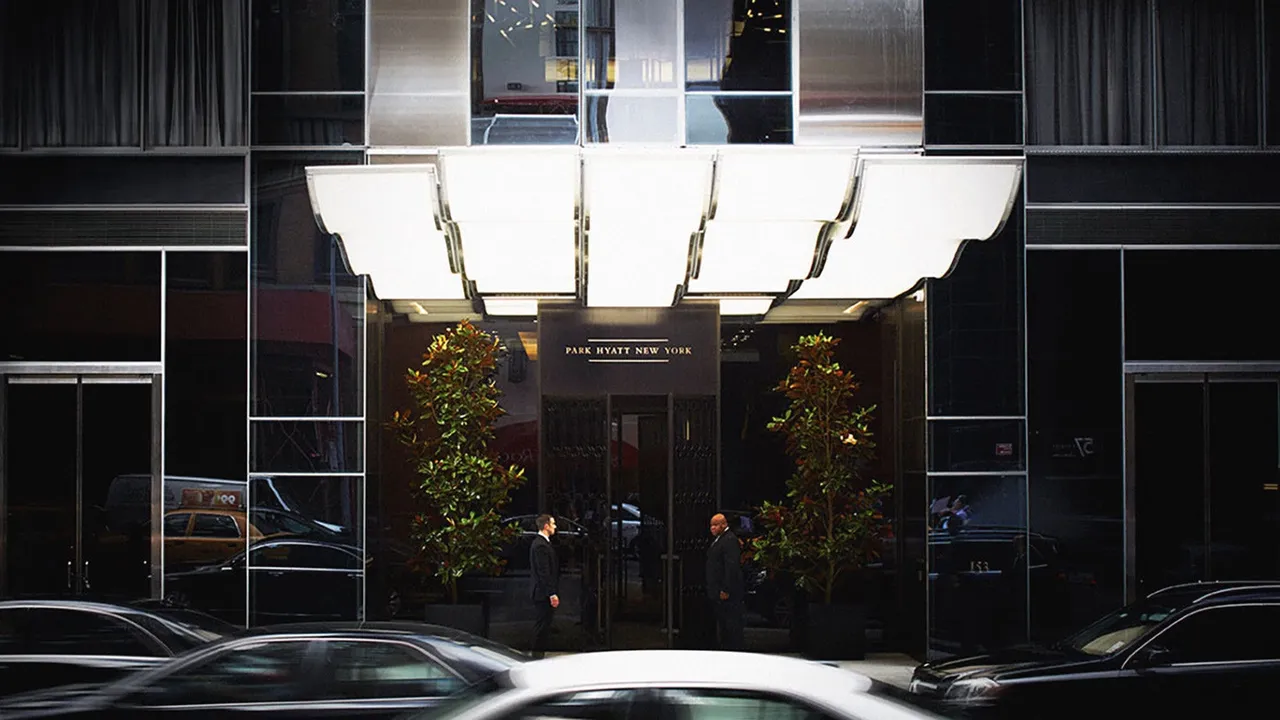 Entrance of Park Hyatt New York with a glowing canopy, doormen and cars passing on the street