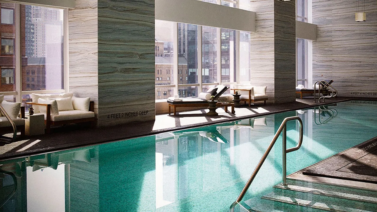 Indoor pool at Park Hyatt New York with stone-clad columns, loungers and tall windows onto Manhattan